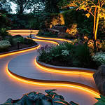 Illuminated winding garden path with plants at dusk.